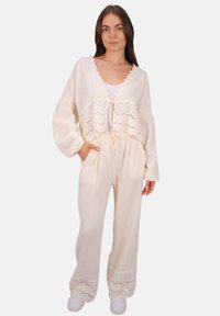 Cremefarbenes, strukturiertes zweiteiliges Outfit bestehend aus einem gekürzten Oberteil mit gewelltem Saum und weit ausgestellten Hosen mit Spitze und Taschen.