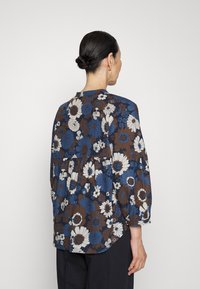 Blusa floreale in tonalità blu e marrone, caratterizzata da un design a peplum, maniche lunghe e un tessuto morbido e leggero con scollo rotondo.