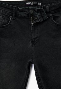 Jeans ajustados negros con cierre de cremallera y botón, que cuentan con bolsillos frontales y un tejido de textura suave. La etiqueta indica la talla W32 L32.