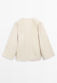 Veste beige avec une texture lisse et mate, des manches larges et un col arrondi. Présente un détail de couture central au dos.