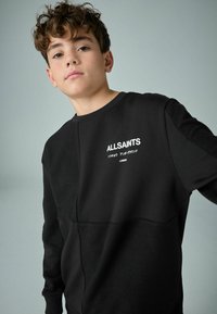 Svart sweatshirt med texturerade paneler och släta ytor. Har "ALLSAINTS"-logotypen i vitt. Rundad halsdesign, ribbade ärmslut och nederkant.