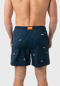 Pantaloni da mare navy con vita elasticizzata, motivi di sushi ricamati e una piccola tasca laterale. Il materiale sembra liscio e leggero.