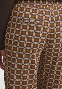 Un pantalon à carreaux marron et jaune avec un tissu texturé, comportant une poche arrière et une finition soignée.
