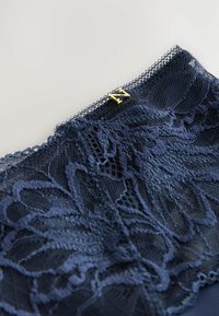 Marineblaue Spitze-Lingerie mit floralen Mustern und einem zarten gewellten Rand, versehen mit einem goldenen Hardware-Element an der Oberseite.