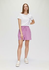 T-shirt blanc avec un petit graphique, associé à un short rose avec cordon de serrage. Le short présente deux poches latérales et une coupe décontractée.