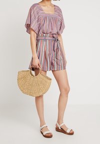 Blouse rayée à manches larges, associée à un short ceinturé. Accessoires comprenant un sac en paille tressée et des sandales blanches à semelles marron.