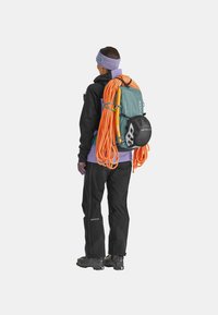 Back view of a person wearing a black jacket, orange climbing rope, and a teal backpack. Person has a purple headband and black trousers.