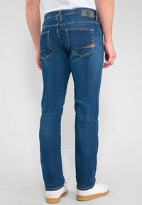 Jean en denim bleu avec une légère décoloration, design à cinq poches et coupe droite. Comprend une étiquette logo sur la ceinture arrière.