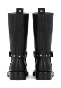 Botas de cuero negro hasta la rodilla con una textura suave, tachuelas metálicas en la correa del tobillo y un resistente tacón cuadrado. Se muestra vista trasera.