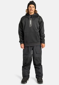 Zwarte hoodie met een voorzak, voorzien van een grafische print. Gecombineerd met losse zwarte cargo-broeken, getextureerd met grote zakken.