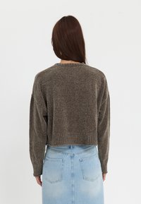 Pull marron court en maille avec manches longues et surface texturée, associé à une jupe en denim bleu clair avec poches arrière.