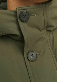 Chaqueta acolchada verde oliva con un cuello alto, que cuenta con un cierre de botones y cremallera, textura suave y detalles de costura.