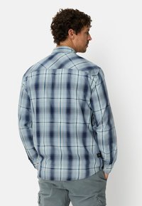 Blau-weiß kariertes Langarmhemd mit Knopfkragen, aus strukturiertem Stoff und mit abgerundetem Saum, getragen zu grauen Shorts.