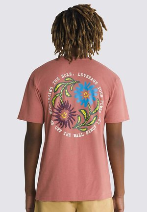 Camiseta de manga corta en color rosa polvo con estampados florales coloridos en azul, púrpura y verde, con un diseño de texto circular en la parte posterior.