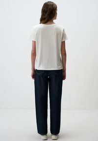 Biała koszulka z krótkim rękawem w połączeniu z ciemnoniebieskimi szerokimi spodniami. Materiał wydaje się miękki, z luźnym krojem i minimalistycznym wzornictwem.