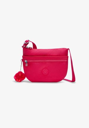 Różowa torebka crossbody z zamkiem błyskawicznym, okrągłym logo i puszystym breloczkiem w kształcie małpki przymocowanym do metalowego zapięcia.