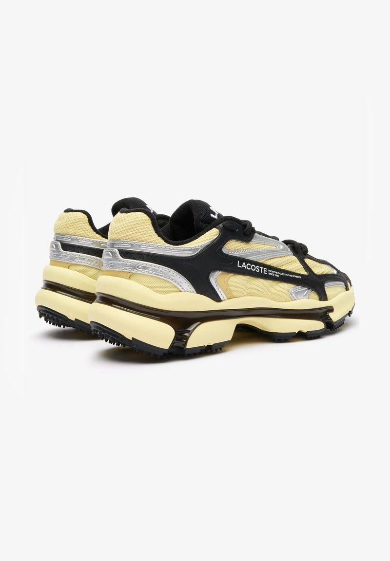 Une paire de baskets Lacoste jaune et noire avec un tissu en maille, des accents argentés réfléchissants et des semelles épaisses et rembourrées, vue d'un angle arrière.