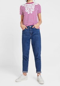 Camiseta a rayas rosa y blanca con detalles de encaje en el escote, combinada con jeans azules de puños doblados y zapatillas blancas.