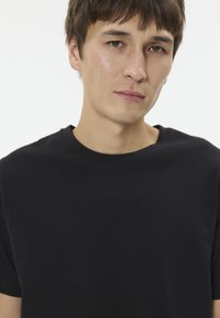 Čierne tričko s okrúhlym výstrihom vyrobené z jemnej, hladkej tkaniny s krátkymi rukávmi a štandardným strihom. Bez viditeľných vzorov alebo kovových prvkov.