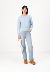 Svijetloplava knit vest sa dugim rukavima, uparen sa svijetloplavim trapericama. Model drži bijelu torbu, nosi smeđe platforme. Jednostavan dizajn.