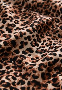 Tkanina s leopardím vzorem ukazuje béžové pozadí s hnědými a černými skvrnami. Textura vypadá měkce a splývavě.