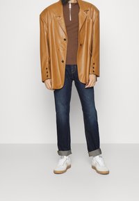 Hnědý sametový kožený oversized blazer, hnědý zipový top, tmavě modré džíny, bílé tenisky s gumovými podrážkami, casual fit, ohrnuté rukávy.