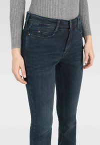 Dunkelblaue Jeans aus Denim mit einer figurschmeichelnden Passform, fünf Taschen und einem Reißverschluss. Der Stoff hat eine glatte Textur mit leichten Verwaschungen.