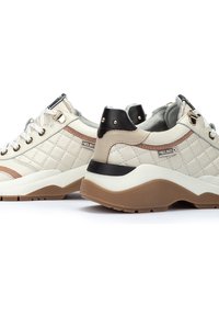 Baskets en toile beige matelassées avec des accents de talon noirs et une bande marron. Présentent des lacets ronds, des œillets en métal et une semelle extérieure blanche épaisse.