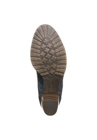 Suela de zapato con un patrón de tachuelas detallado, material de goma, forma redondeada y un pequeño tacón de madera. El color es marrón oscuro con un acabado texturizado.