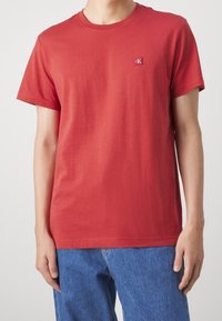 Rød bomulds t-shirt med korte ærmer, rund Halsudskæring og et lille broderet logo på brystet, parret med blå denim jeans.