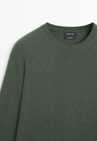 Grön crewneck-tröja tillverkad av 100 % kashmir. Mjuk textur med ribbad halsringning. Etikett synlig mitt bak på nacken.