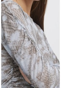 Långärmad topp i lätt tyg med grått och beige ormmönster, med samlade detaljer på ärmarna för textur.