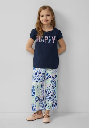 Marineblauwe katoenen t-shirt met de tekst "HAPPY" in roze en blauwe patronen, gecombineerd met brede bloemenprintbroek in pastelkleuren. Roze platte schoenen.