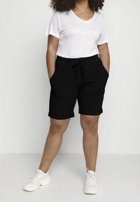 Black, mid-length shorts with a drawstring waist, featuring side pockets and rolled cuffs. Paired with a plain white v-neck t-shirt and white sneakers.