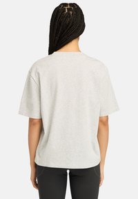 Šedé bavlněné tričko s volným střihem, krátkými rukávy a kulatým výstřihem. Pohled ze zad s hladkým, texturovaným materiálem.