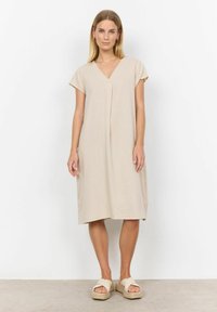 Beiges kurzärmliges Kleid mit V-Ausschnitt und Falten-Detail. Das Material wirkt leicht und strukturiert. Kombiniert mit Plateau-Sandalen.