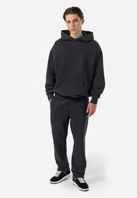 Black hoodie and matching pants made of soft fabric. Hoodie features a front pocket and ribbed cuffs. Sneakers with black and white accents.