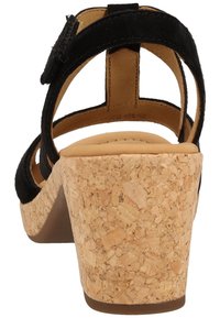 Sandale compensée en suède noir avec plateforme en liège et arrière solide. Comprend une bride de cheville ajustable et une semelle rembourrée pour plus de confort.