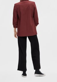 Blazer bordeaux à coupe structurée, manches trois-quarts, associé à un pantalon noir large à côtes et des baskets noires montantes.