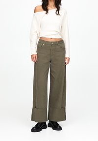 Olivengrønne bredbenede bukser med en cropped snit, featuring en rå afslutning og fem lommer, pari med en hvid off-shoulder sweater.