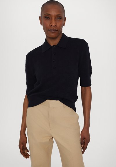 Polo marin cu mâneci scurte, cu un design texturat, având un guler clasic și o închidere cu nasturi, asortat cu pantaloni bej, pe măsură.