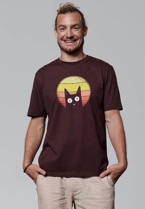 Maroon cotton T-shirt featuring a cartoon cat design against a sunburst of yellow and orange stripes. Short sleeves and crew neck.