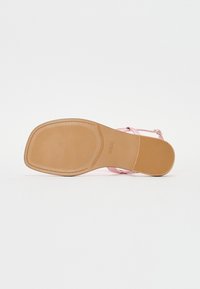 Rosa högklackad sandal med en slät, glänsande yta, med korsande remmar och en platt, texturerad tan sula, märkt "GUESS."