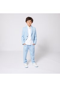 Hellblaues Anzugset aus Jacke und Hose, mit einem weißen Hemd darunter und weißen Sneakers. Glatte Stofftextur und moderne Designdetails.