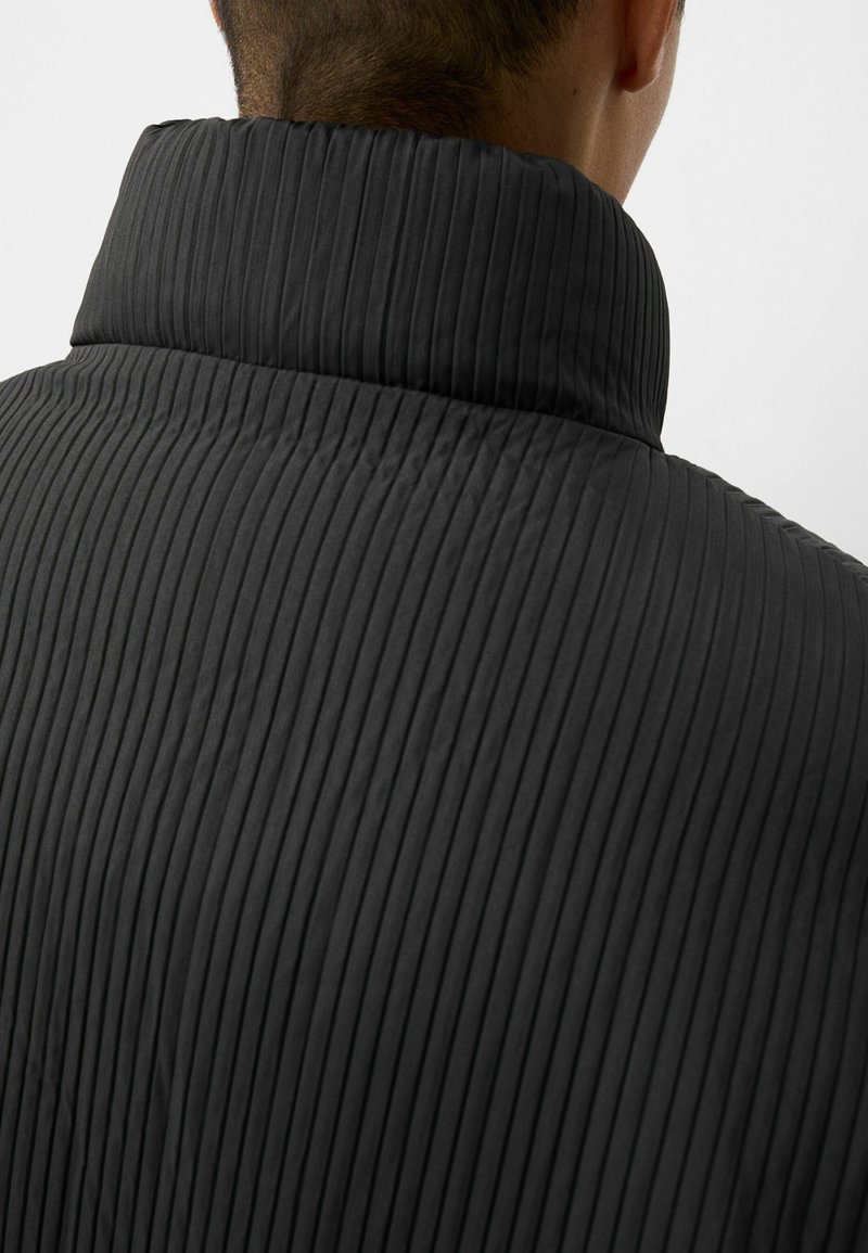 Schwarze, gesteppte Jacke mit hohem Kragen und vertikaler Rippstruktur, ausgestattet mit einer glatten Oberfläche und strukturiertem Design.