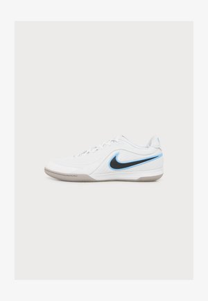 Άσπρο sneaker Nike χαμηλής κοπής με μαύρο και γαλάζιο λογότυπο swoosh, λευκά κορδόνια και μπεζ σόλα σε απλό ανοιχτό φόντο.