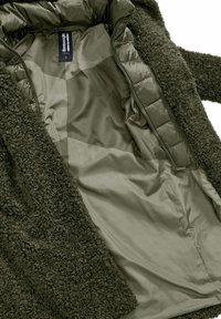 Groene buitenkleding met een gestructureerde, harige buitenkant. Het binnenfutter is glad en mat. Beschikt over een rits en een label aan de binnenkant.