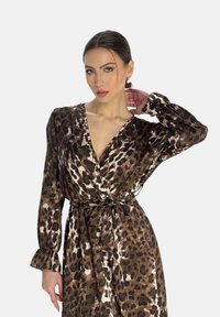 Robe imprimée léopard en marron et blanc, avec un décolleté en V profond, des manches longues avec des poignets élastiques et un détail de taille nouée. Texture de tissu douce.