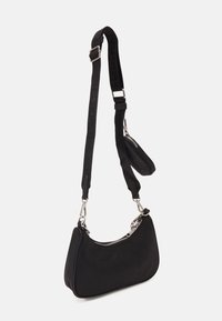 Bolso de hombro negro en forma de media luna con cremallera plateada y correa ajustable y desmontable, sobre fondo blanco liso.