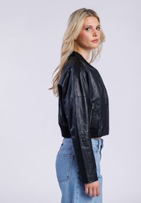 Černá kožená krátká bomber bunda s žebrovanými manžetami a lemem, předním zipovým zapínáním a boční kapsou na zip. Neformální design s hladkým povrchem.